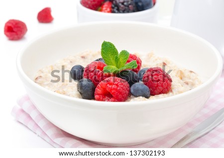 healthy breakfast - oatmeal with fresh berries in a bowl isolated on white, fresh berries in the background, horizontal closeup