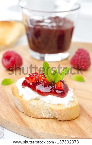 piece of toasted baguette with cream cheese, raspberry jam and raspberries on a wooden board