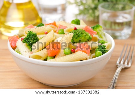 salad with pasta, smoked salmon, broccoli and green peas in a white bowl on a wooden table