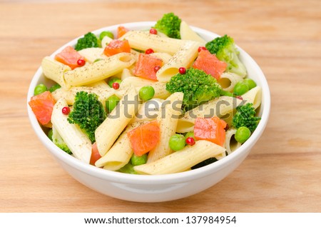 salad with pasta, smoked salmon, broccoli and green peas in a white bowl on a wooden table, horizontal top view