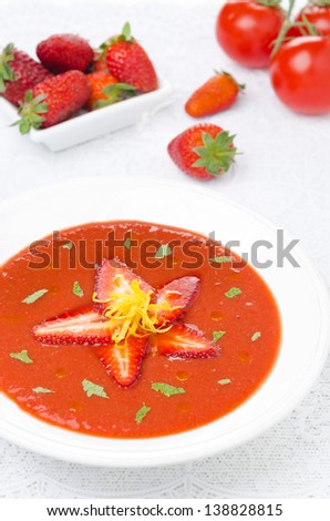tomato and strawberry gazpacho in a plate, fresh berries and tomatoes in the background, vertical