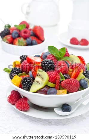 salad of fresh fruit and berries in a white bowl, berries and a cup of tea in the background, vertical