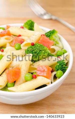 salad with pasta, smoked salmon, broccoli and green peas in a white bowl on a wooden table, top view