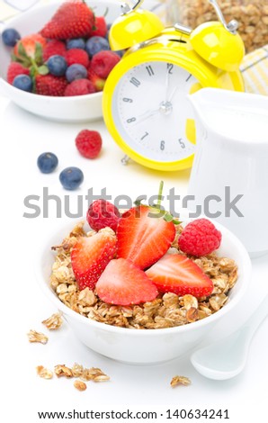 Granola with fresh berries and milk for breakfast and yellow alarm clock on a white background