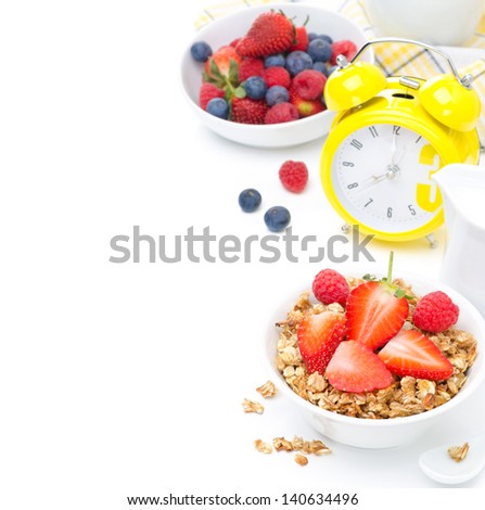 breakfast with granola, fresh berries, milk and yellow alarm clock on white