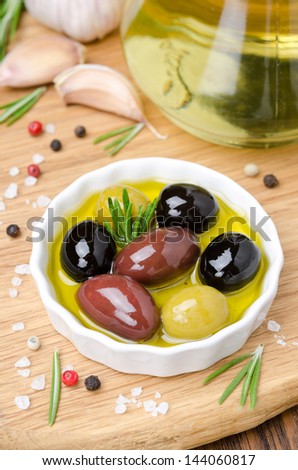 three varieties of olives in a bowl with olive oil and spices on a wooden board, close-up