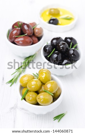 three kinds of olives, fresh rosemary and olive oil on a white background