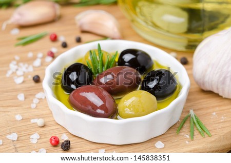 bowl with different olives in olive oil and spices on a wooden board, horizontal