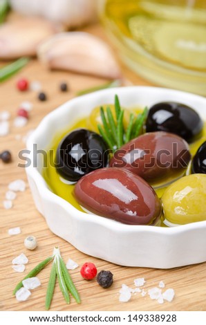 close-up of a bowl with olives in olive oil and spices on a wooden board, vertical
