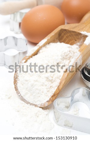 scoop with wheat flour, rolling pin, eggs and cookie cutters isolated on white, close-up