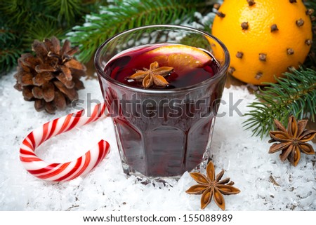 spicy mulled wine in the glass on the snow and caramel candy, horizontal