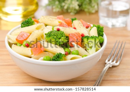 salad with pasta, smoked salmon, broccoli and green peas in a white bowl on a wooden table horizontal