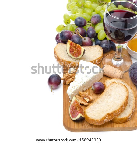 snacks - cheese, bread, figs, grapes, nuts and a glass of wine on a wooden board, isolated on white