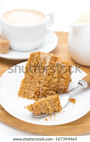 piece of honey cake on a plate, fork and cup of cappuccino on wooden board, close-up, vertical