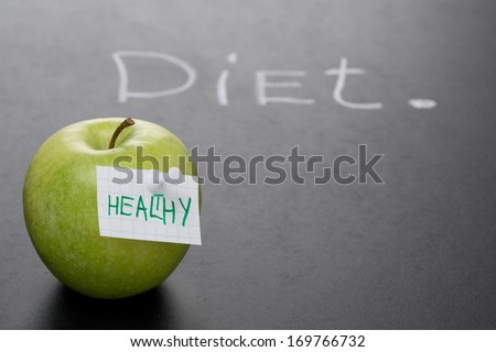 green apple with label on a dark background and the word diet, written in chalk, close-up