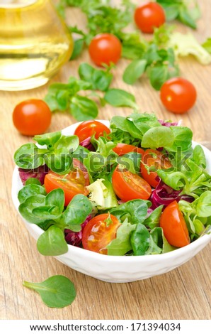 bowl of fresh salad and cherry tomatoes in a white bowl on a wooden background, vertical close-up
