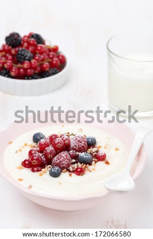 semolina porridge with fresh berries, nuts and glass of milk, vertical
