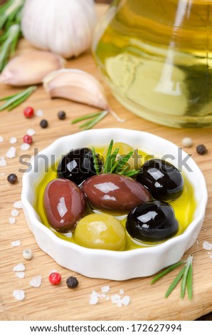 three kinds of olives in a bowl with olive oil and spices on a wooden board, vertical