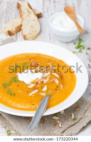 carrot soup with almonds, yogurt and watercress in a plate, vertical, close-up