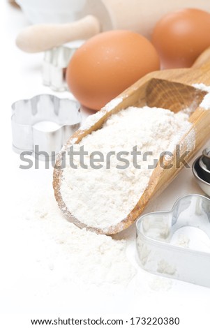 scoop with wheat flour, rolling pin, eggs and cookie cutters isolated on white background
