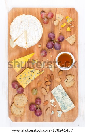 assorted soft cheeses, grapes, nuts and honey on a wooden cutting board, top view, vertical
