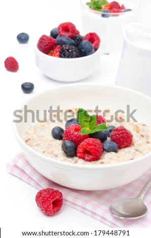 healthy breakfast - oatmeal with fresh berries in a bowl isolated on white, fresh fruit, yogurt, and milk jug in the background