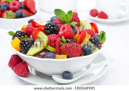 salad of fresh fruit and berries in a white bowl, berries and a cup of tea in the background, horizontal