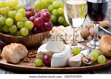 Camembert, fresh baguette, grapes and wine on a wooden tray, horizontal