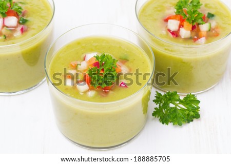 green soup with fresh vegetables in glasses, top view, close-up