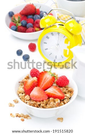 breakfast with granola, fresh berries and yellow alarm clock isolated on white background