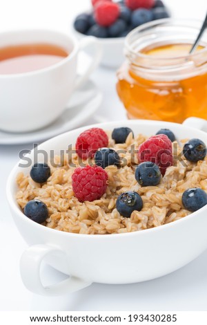 breakfast - oat porridge with fresh berries and honey, black tea, vertical, close-up