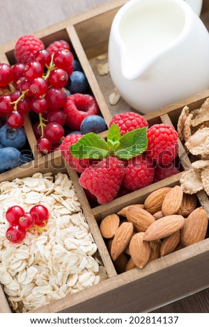 box with breakfast items - oatmeal, granola, nuts, berries and milk, close-up, vertical
