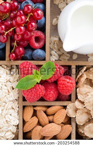 foods for breakfast - oatmeal, granola, nuts, berries and milk in wooden box, top view, vertical, close-up