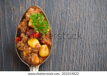 spicy Mexican dish chili con carne in a spoon on wooden background, concept photo, close-up