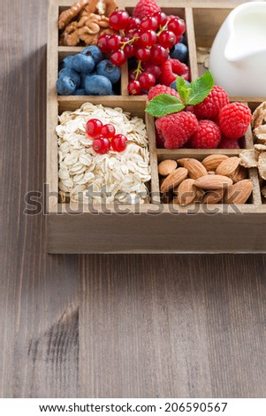 box with breakfast items - oatmeal, granola, nuts, berries and milk on wooden table, vertical, top view