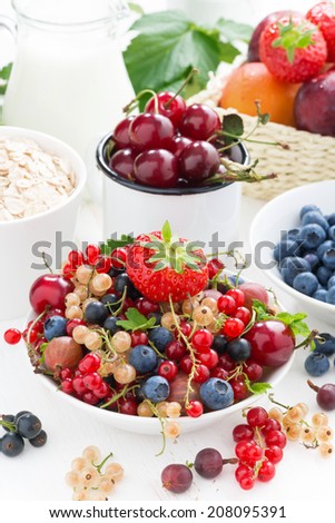 fresh berries, fruit, cereal and milk for breakfast on white table, close-up, vertical