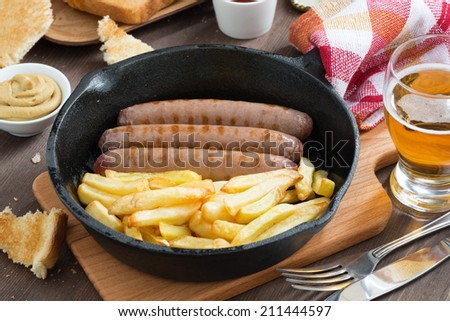 grilled sausages with French fries  in a frying pan, toasts and beer, top view, horizontal