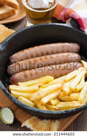 grilled sausages with French fries in a frying pan, vertical, close-up