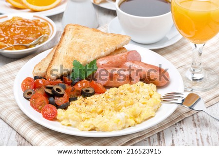 scramble eggs with tomatoes, sausage and toast on a plate for breakfast, close-up