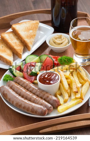 lunch with grilled sausages with French fries, vegetables and beer, vertical, close-up