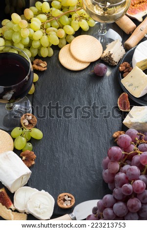 black background with cheeses, grapes, crackers and wine, top view, vertical