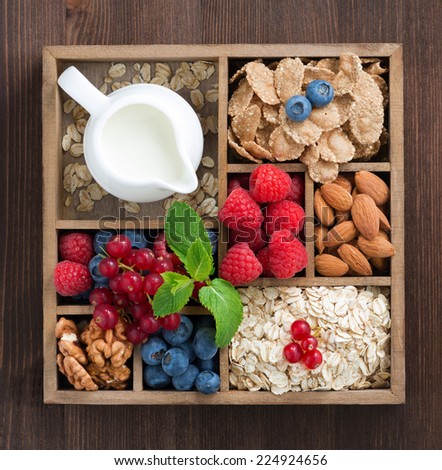 wooden box with breakfast items - oatmeal, granola, nuts, berries and milk, top view, close-up