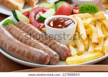 lunch with grilled sausages, French fries, vegetables and beer, close-up, horizontal