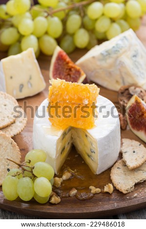 camembert with honey and fruit, snacks on a wooden tray, vertical, close-up