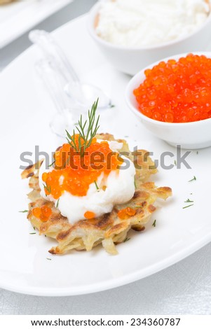 potato pancakes with red caviar and sour cream on the plate, close-up, vertical