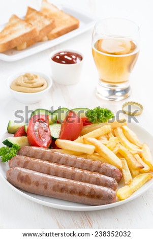 grilled sausages with French fries, vegetables and glass of beer, vertical