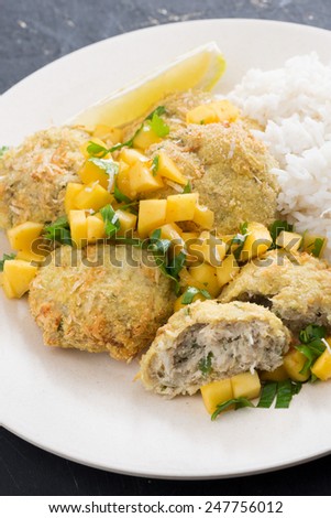 Thai fish cakes with mango salsa and rice on a plate, close-up, vertical
