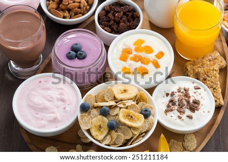 rich breakfast buffet with cereals, yoghurt and fruit on wooden tray, top view horizontal, close-up