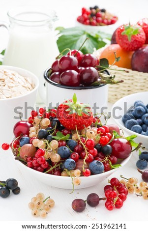 fresh berries, fruit, cereal and milk for breakfast on white table, vertical
