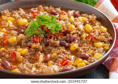 spicy Mexican dish chili con carne in a brown pottery plate, close-up, horizontal